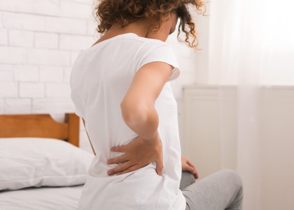 mulher sentada na cama com as mãos na lateral com dor nas costas
