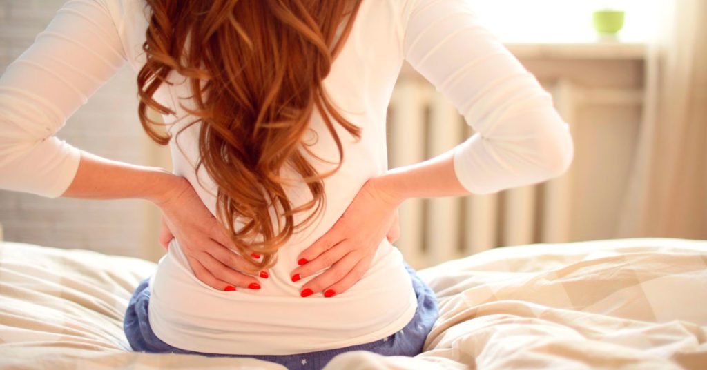 mulher sentada na cama com dor nas costas