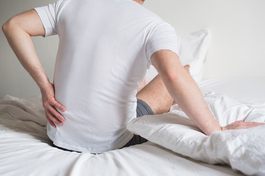 homem sentado na cama com dor nas costas ao acordar