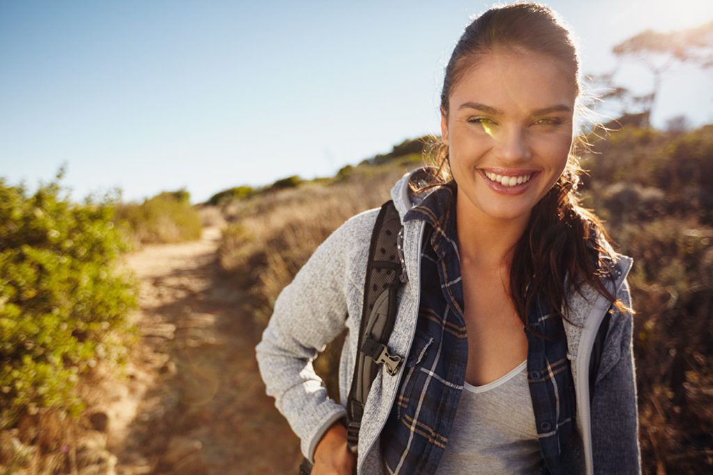 menina com dor nas costas ao caminhar pelas montanhas
