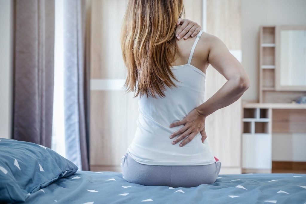 mulher sentada na cama com dor nas costas ao acordar