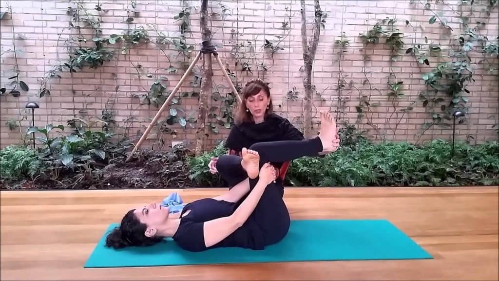 Sessão de fisioterapia para lombar com uma profissional auxiliando a paciente em um exercício de alongamento para alívio da dor.