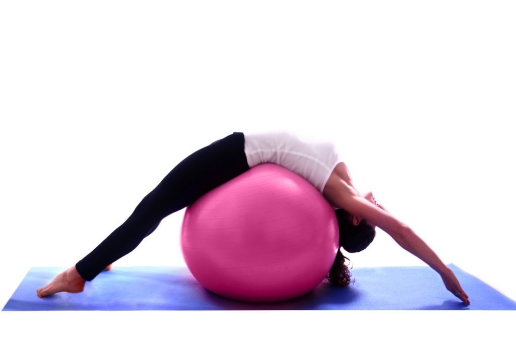 mulher deitadade costas sobre bola de pilates fazendo exercícios pra hipercifose