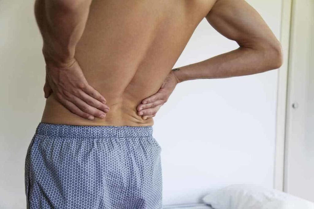homem sem camisa de costas com as mãos na lombarcom dor por cistos de tarlov