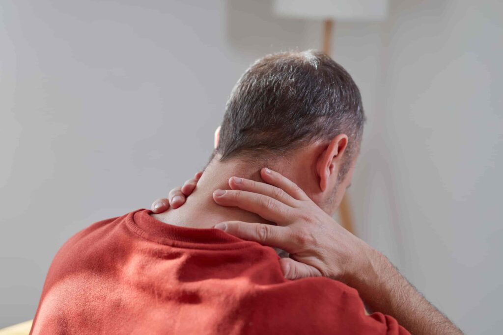 Homem com dor no pescoço massageando a nuca, um sintoma comum de hérnia de disco cervical ou outras condições da coluna. A imagem destaca a importância de reconhecer os sintomas de hérnia de disco.