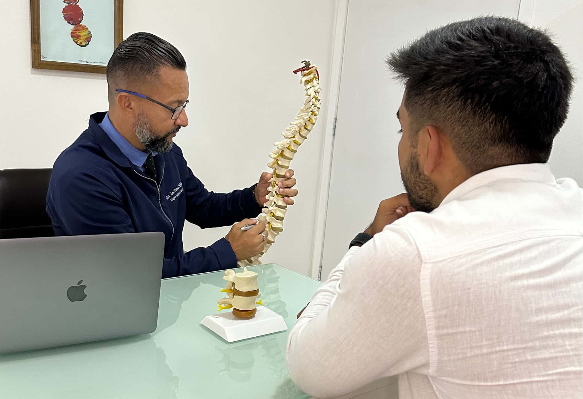 Fisioterapeuta explicando para o paciente o modelo de uma coluna vertebral, abordando problemas musculoesqueléticos e tratamento para dor nas costas.