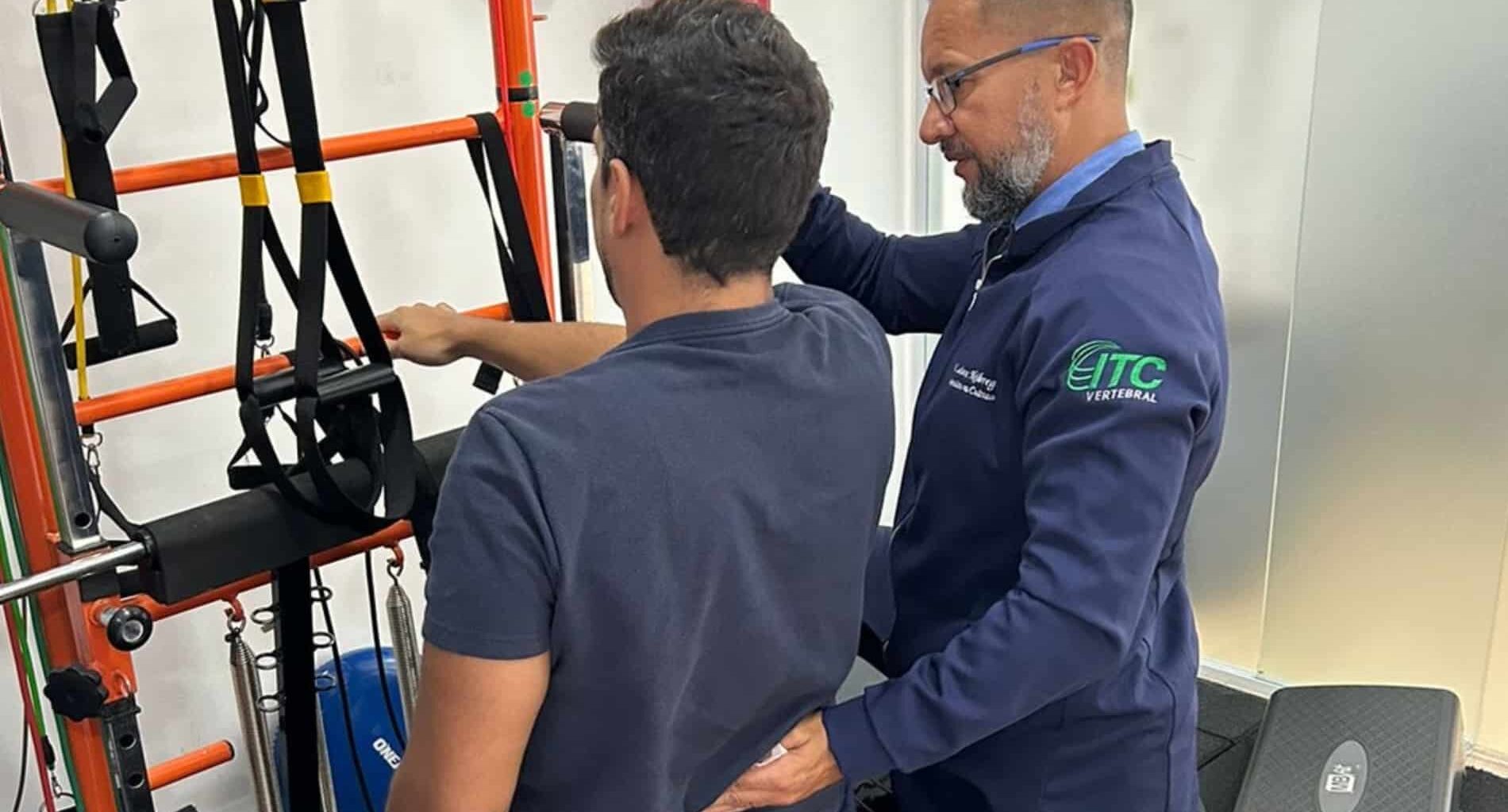 Um fisioterapeuta do ITC Vertebral orientando um paciente durante exercícios de fisioterapia para coluna em um equipamento de Pilates.